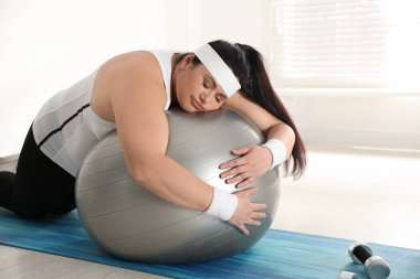 Spor salonunda antrenman yapmak yerine formda topa yaslanan tembel şişman kadın.