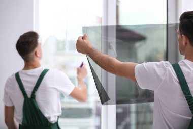 Professional workers tinting window with foil indoors clipart