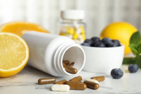 Bottle with vitamin pills, blueberries and lemon on white marble table