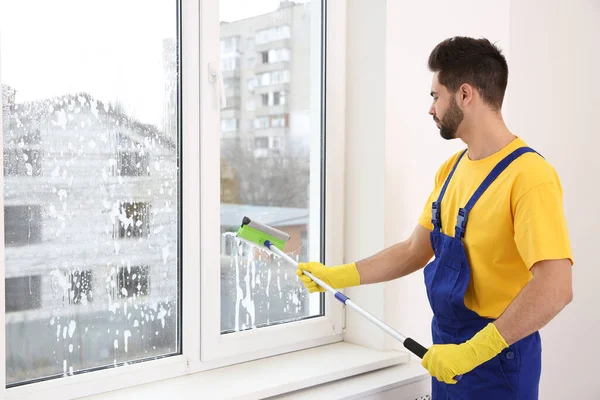 室内制服清洗窗的年轻专业看门人 — 图库照片