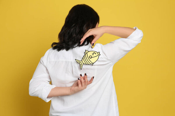 Woman with paper fish on back against yellow background. April fool's day