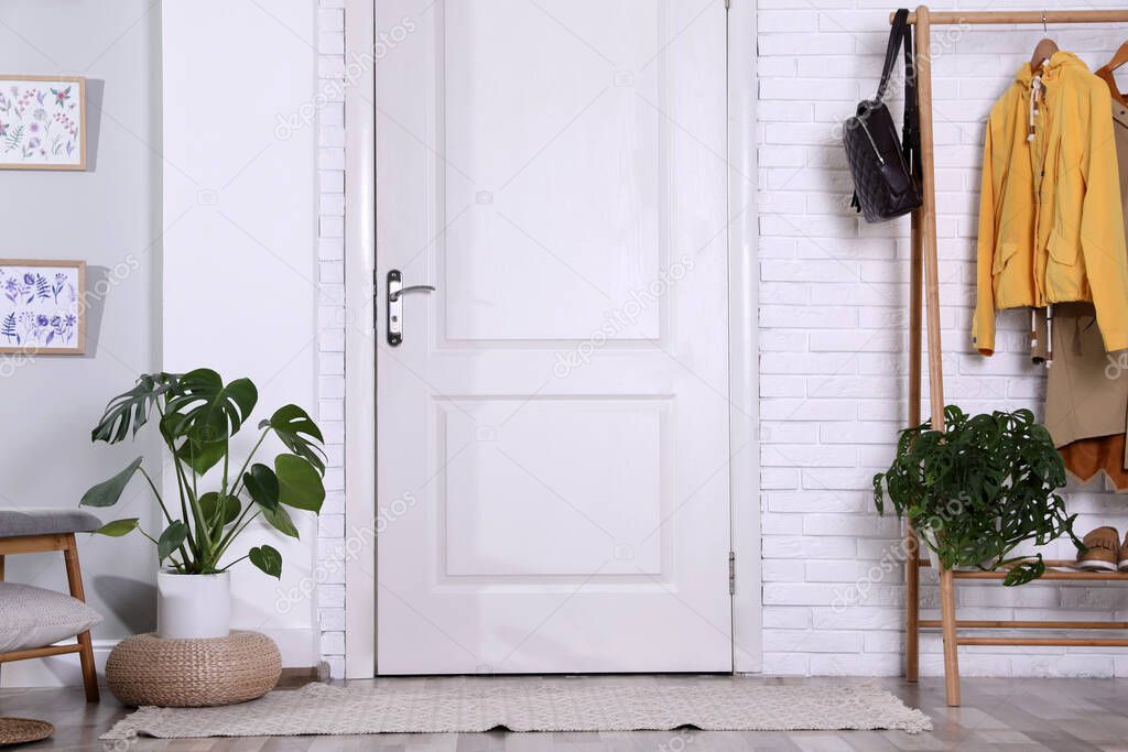 Hallway interior with stylish furniture, clothes and plants