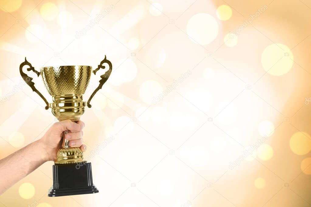 Man holding gold trophy cup on color background, closeup. Space for text