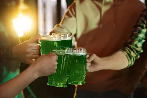 Group of friends toasting with green beer in pub, closeup. St. Patrick\'s Day celebration