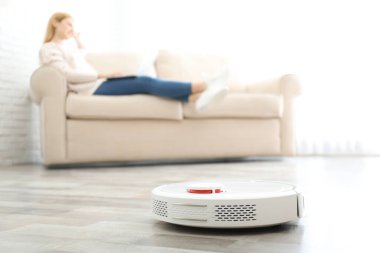 Robot elektrik süpürgesi evde çalışırken dinlenen bir kadın.