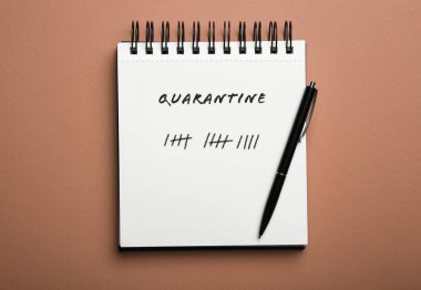 Kahverengi arkaplandaki defter ve kalemi aç, üstten bak. Coronavirüs salgını sırasındaki karantina günleri sayılıyor