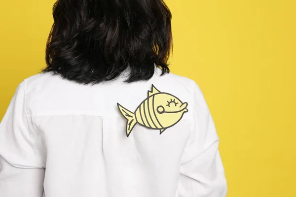 黄色の背景に背を向けて紙の魚を持つ女性 クローズアップ 4月のバカの日 — ストック写真