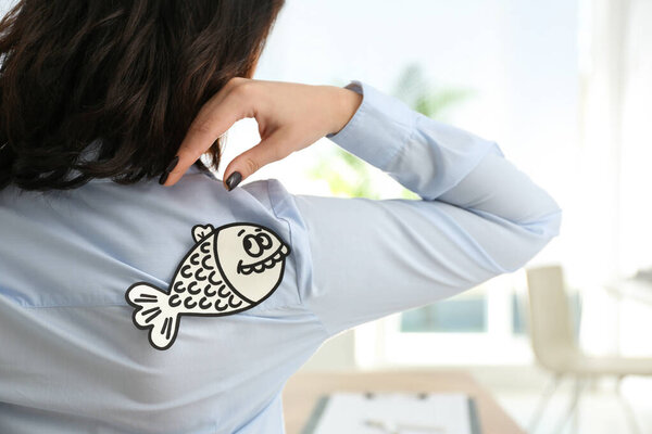 Woman with paper fish on back indoors, closeup. April fool's day