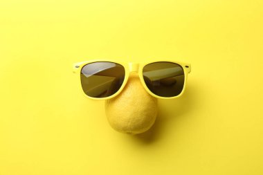 Sarı arka planda sulu limon ve güneş gözlüğü.