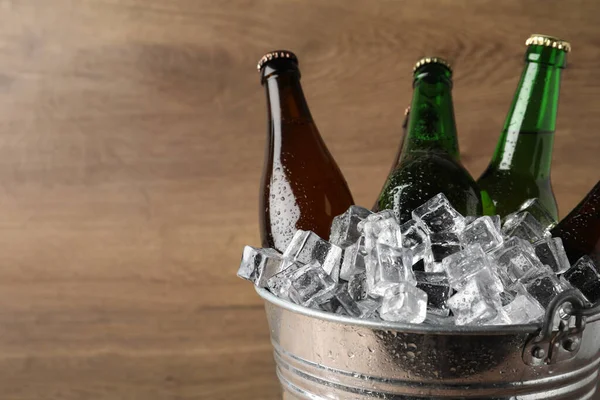 Metal bucket with beer and ice cubes on wooden background. Space for text