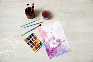Açık masa üzerinde suluboya boya boya ve çiçek resmi olan düz bir kompozisyon.