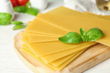 Pişmemiş lazanya çarşafları ve fesleğen beyaz ahşap masada, yakın plan.