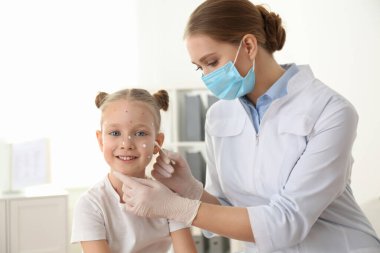 Doktor, klinikte suçiçeği olan küçük bir kızın cildine krem sürüyor. Varicella zoster virüsü