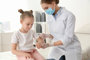 Doktor, klinikte suçiçeği olan küçük bir kızın cildine krem sürüyor. Varicella zoster virüsü