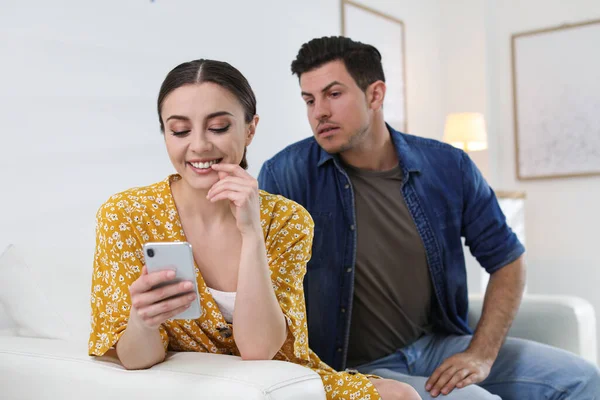 自宅でガールフレンドのスマートフォンに目を凝らしている男 関係における嫉妬 — ストック写真