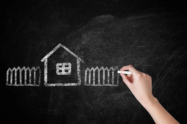 Woman drawing house with fence on chalkboard, closeup