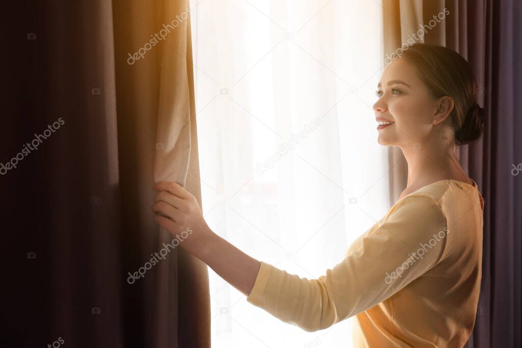 Woman opening window curtains at home in morning