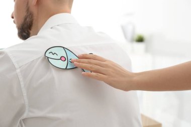 Ofisteki meslektaşına kağıt balığı yapıştıran kadın, yakın plan. 1 Nisan şakası