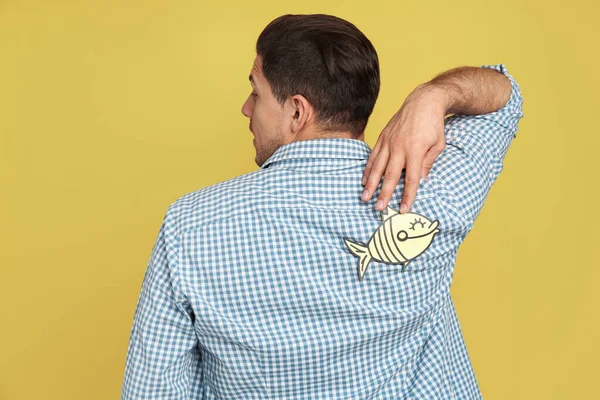 黄色の背景に背を向けて紙の魚を持つ男 4月のバカの日 — ストック写真