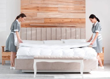 Genç oda hizmetçileri otel odasında yatak yapıyor.