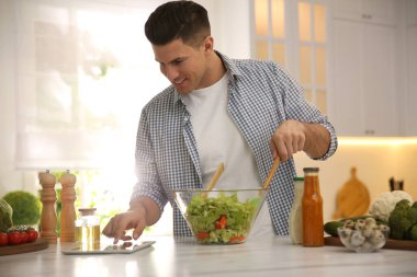 Mutfakta tabletli bir adam salata pişiriyor.