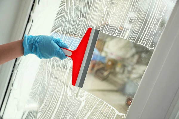 Woman cleaning window with squeegee indoors, closeup