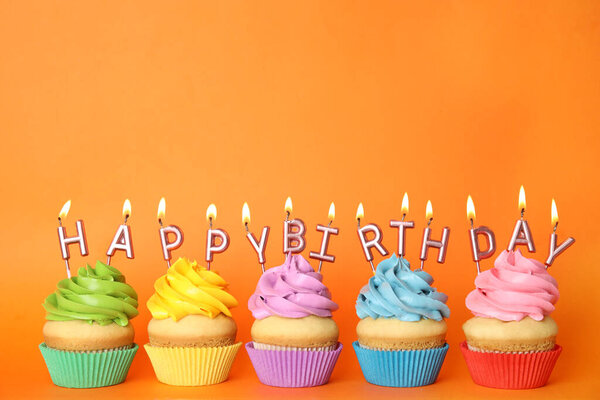 Birthday cupcakes with burning candles on orange background. Space for text