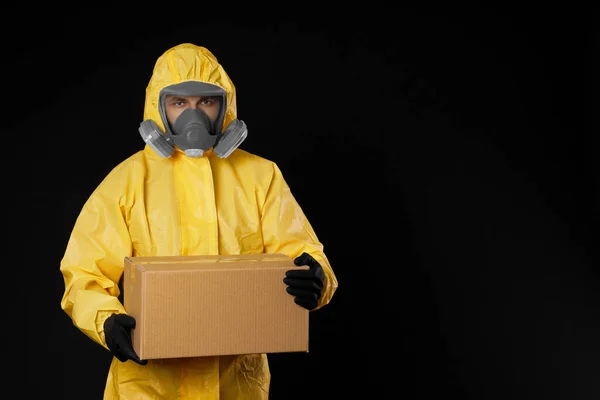 黒の背景に段ボール箱付きの化学保護スーツを着た男 テキストのためのスペース ウイルスの拡散防止 — ストック写真