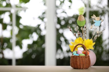 Hasır sepetin içinde Paskalya yumurtalarının bulunduğu şölen kompozisyonu bulanık pencereye karşı masada, metin için boşluk