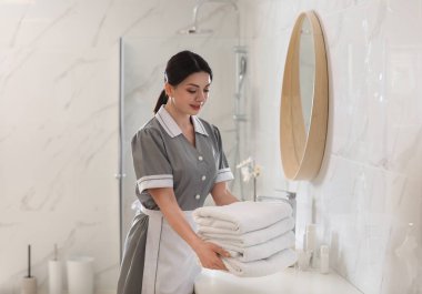 Genç oda hizmetçisi banyodaki tezgahın üstüne temiz havlu yığıyor.