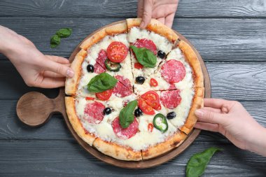 İnsanlar ahşap masada leziz pizza parçaları alıyor.