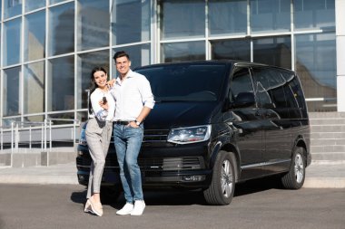 Şehir caddesinde arabasının yanında anahtarı olan mutlu çift. Yeni otomatik alınıyor