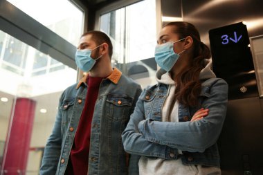 Asansörde tek kullanımlık maskeler takan bir çift. Tehlikeli bir virüs.