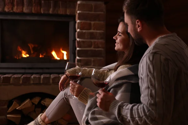 Lovely couple with glasses of wine near fireplace at home. Winter vacation