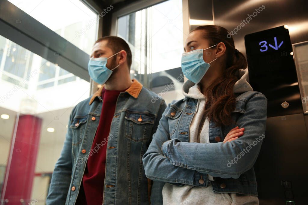 Couple wearing disposable masks in elevator. Dangerous virus