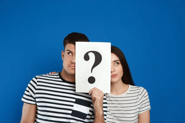 Couple holding question mark sign on blue background