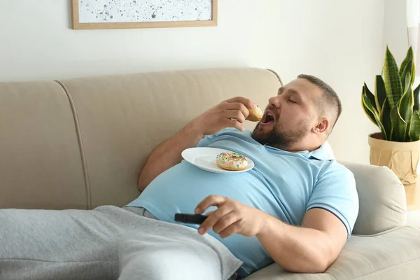 懒散的超重男人 带着甜甜圈在沙发上看电视 — 图库照片