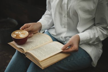 Elinde kahve fincanı olan kadın kitap okuyor, yakın plan.