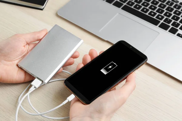 Woman charging mobile phone with power bank at wooden table, closeup