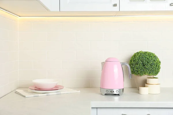 Modern electric kettle, dishes and houseplant on counter in kitchen