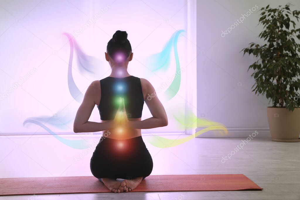 Young woman with chakra points practicing yoga in studio, back view. Healing energy 