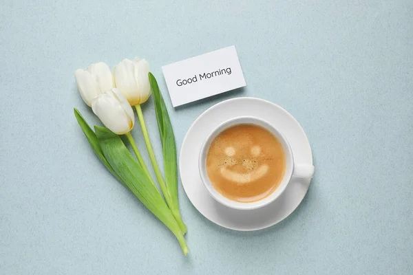 White tulips, coffee and card with Good morning wish on light blue background, flat lay