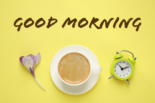 Good Morning. Delicious morning coffee, alarm clock and flower on yellow background, flat lay