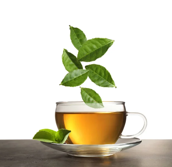 Πράσινα Φύλλα Που Πέφτουν Φλιτζάνι Τσάι Στο Τραπέζι Λευκό Φόντο — Φωτογραφία Αρχείου
