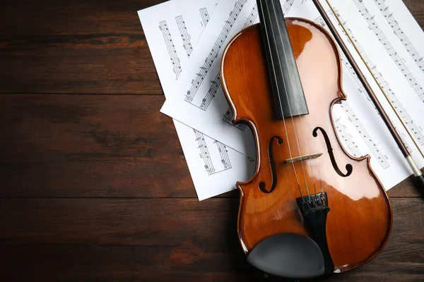 Beautiful violin, bow and note sheets on wooden table, flat lay. Space for text
