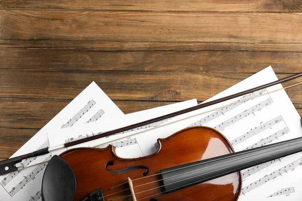 Beautiful violin, bow and note sheets on wooden table, flat lay. Space for text