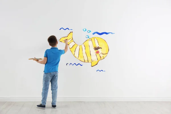 Little child drawing yellow whale on white wall indoors