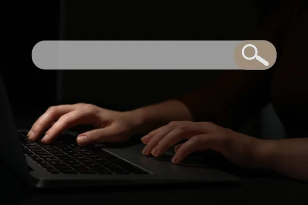 Search bar of internet browser and woman working with laptop in darkness, closeup