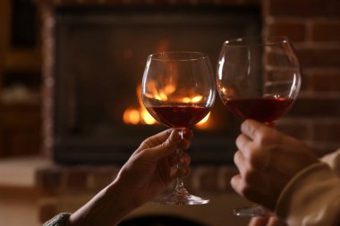 İçeride şöminenin yanında şarap bardakları olan sevimli bir çift, yakın plan. Kış tatili