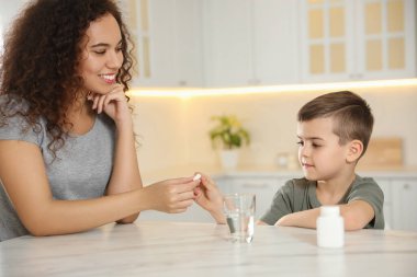 Afro-Amerikalı kadın mutfaktaki küçük çocuğa vitamin hapı veriyor.
